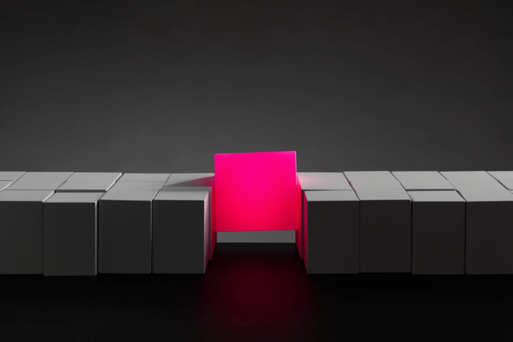 Identical grey cubes with one coral cube stepping forward on a dark surface.