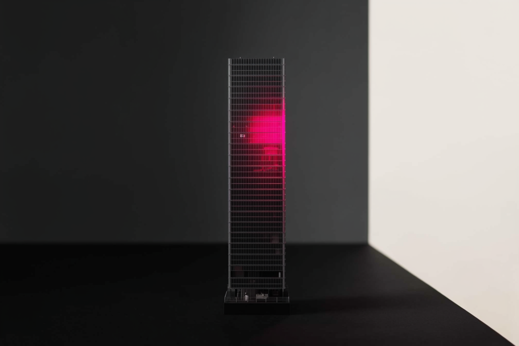 A glass-tower model on a dark surface with a coral-lit face.