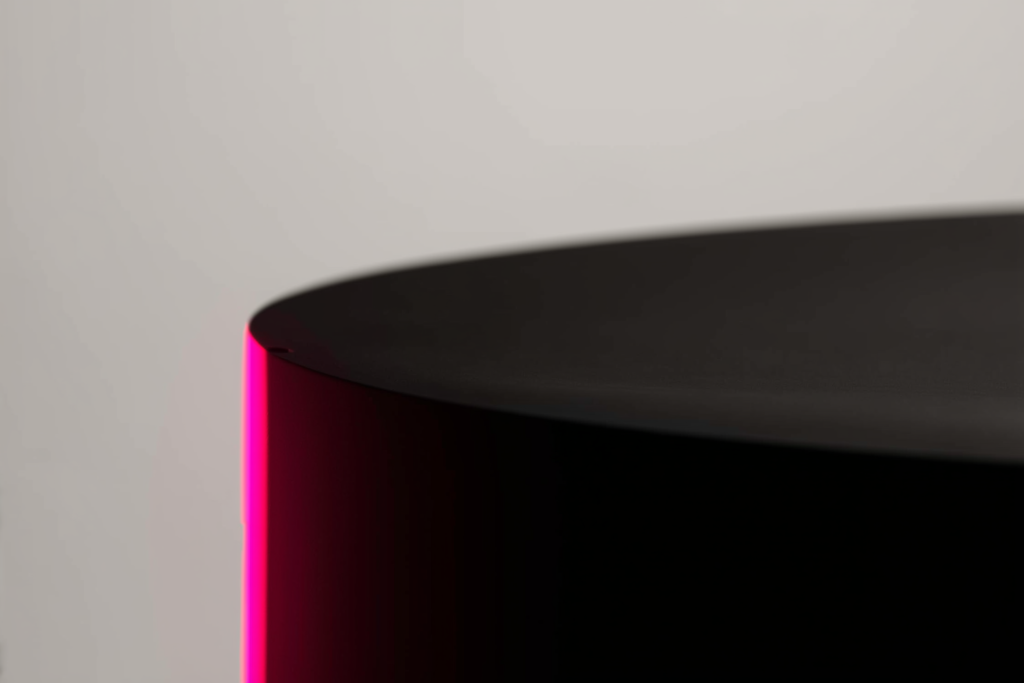 A minimalist architectural model on a dark surface with a coral accent light.
