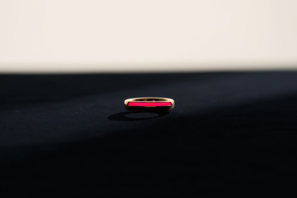 A gold ring on dark velvet with a coral rim light.