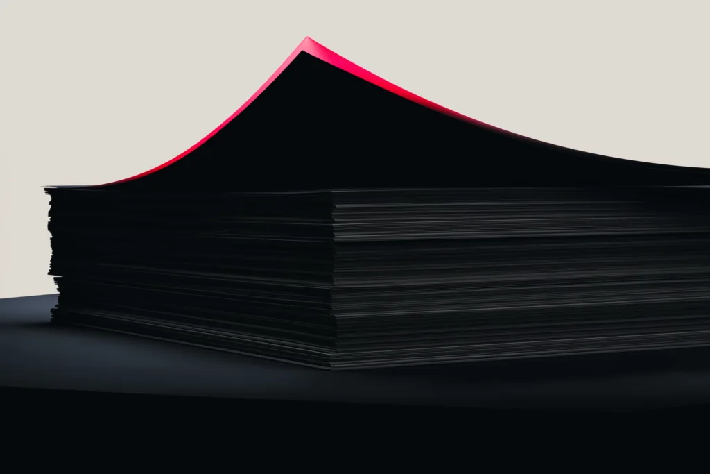 A stack of reports on a dark surface with a coral accent on the top edge.
