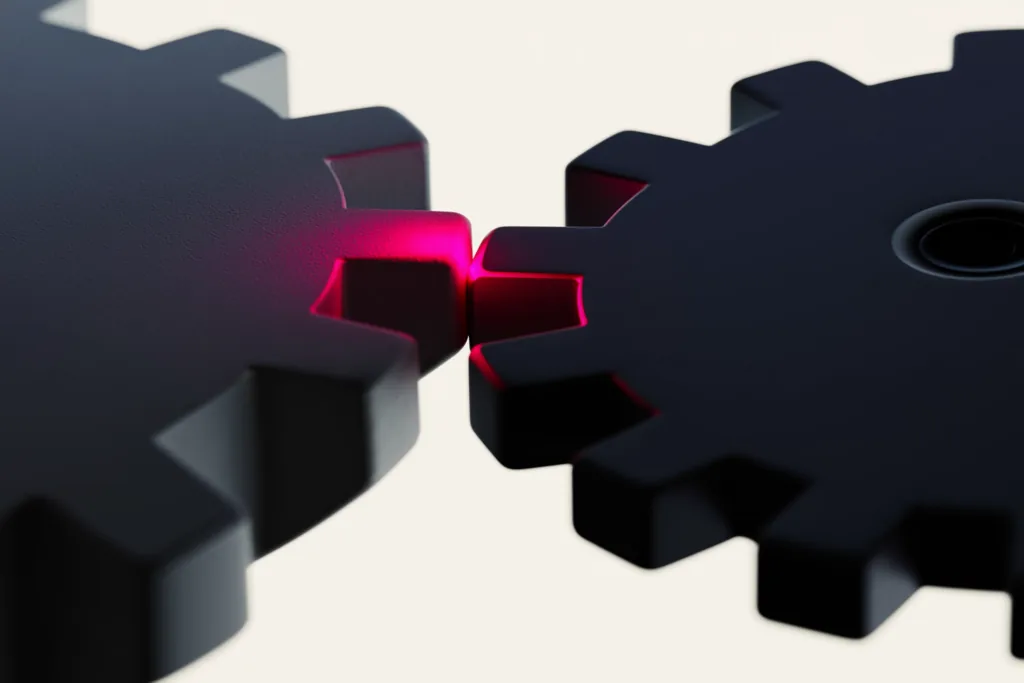 Two meshing gears on a dark surface, one rimmed in coral light.