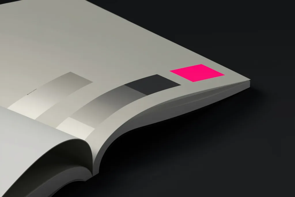 An open brand guidelines book on a dark surface with one glowing coral colour swatch.