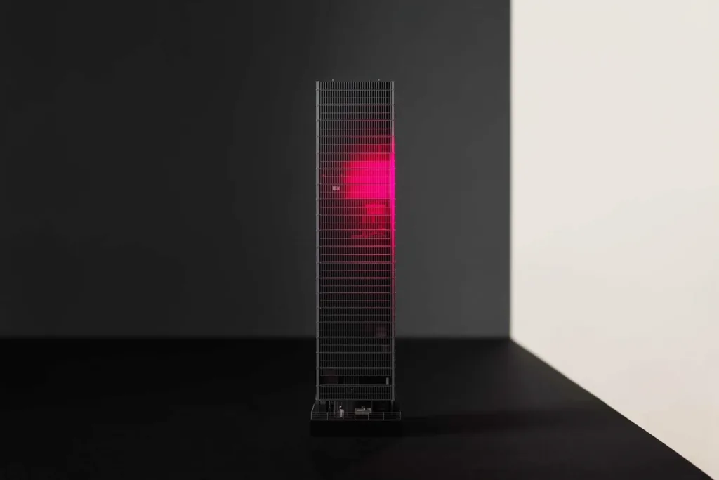 A glass-tower model on a dark surface with a coral-lit face.