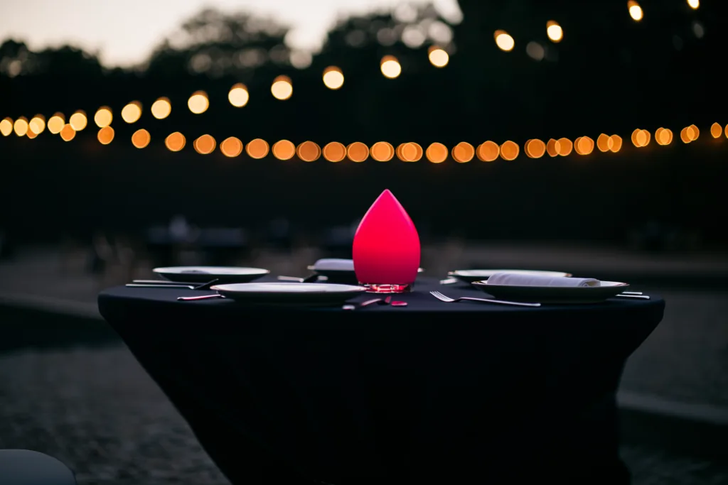An elegant event table setting at dusk with warm bokeh and a coral accent glow.