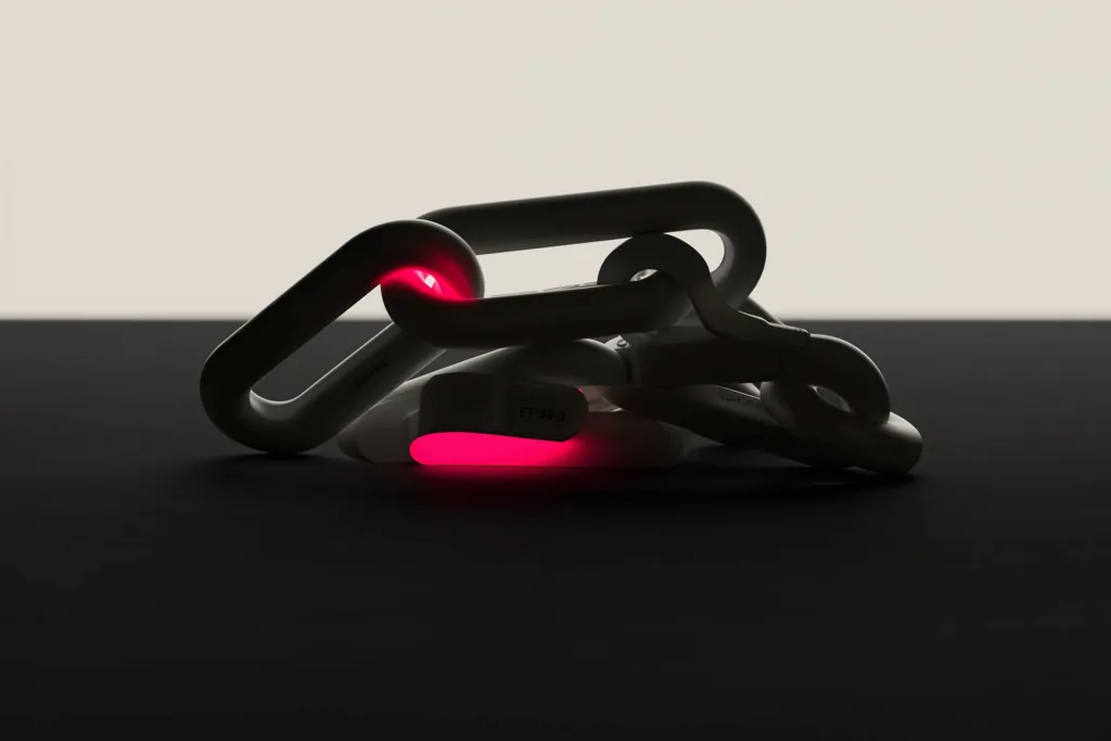 Interlocking chain links with one glowing coral link on a dark surface.