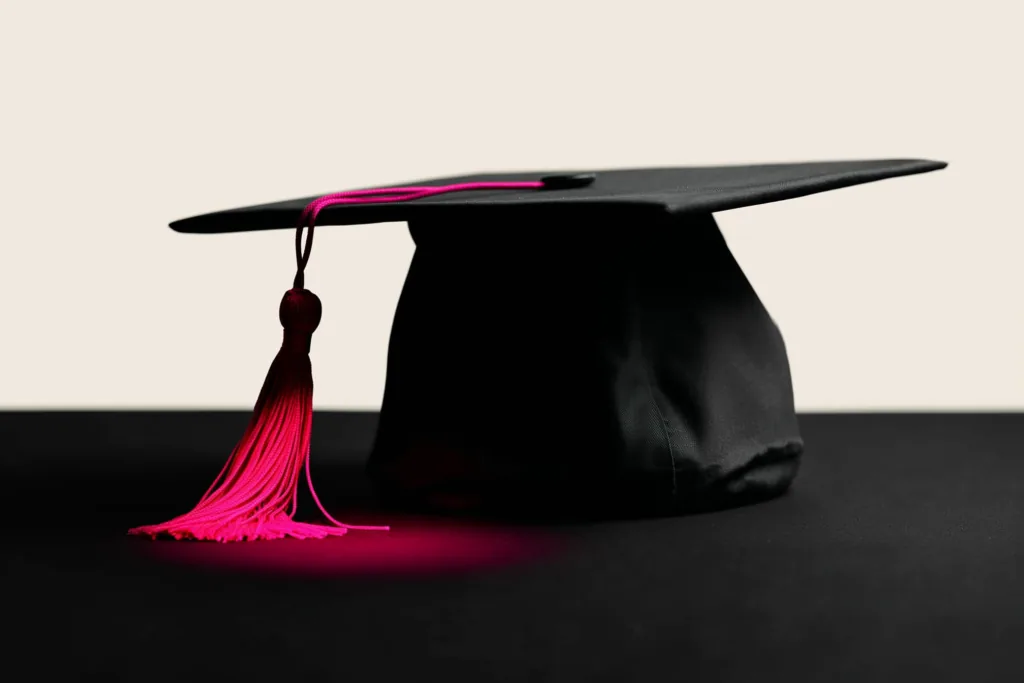 A graduation cap on a dark surface with a coral accent on the tassel.