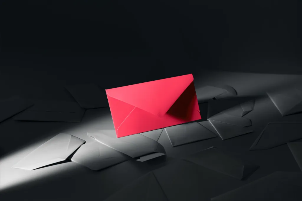 A glowing coral envelope among dark envelopes on a dark surface.