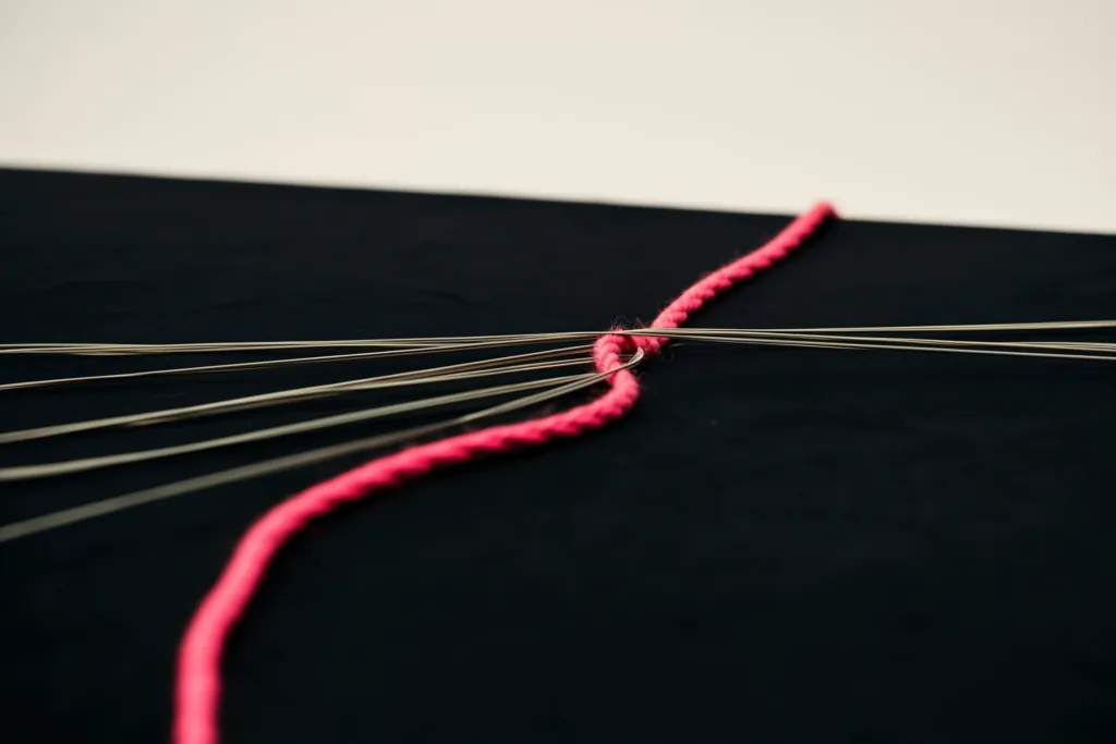 Muted threads braiding into one coral rope of light on a dark surface.