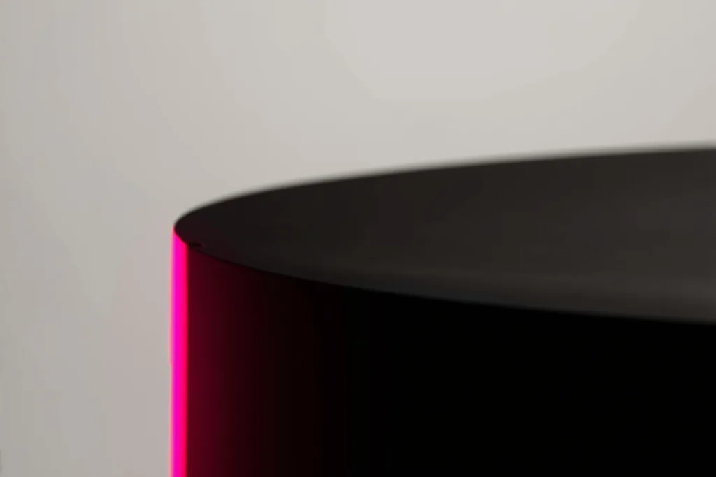 A minimalist architectural model on a dark surface with a coral accent light.