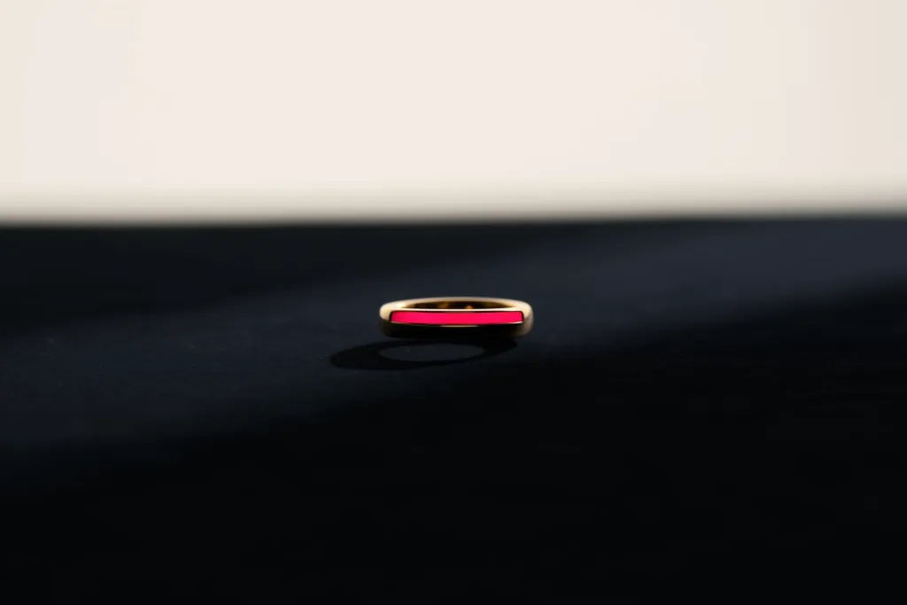 A gold ring on dark velvet with a coral rim light.