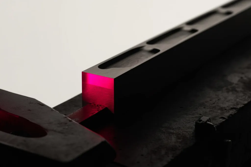 A machined metal component on a dark workshop surface with a coral accent light.