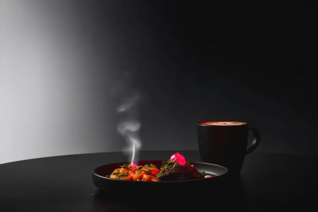 A plated dish on a dark café table with a coral accent glow and rising steam.