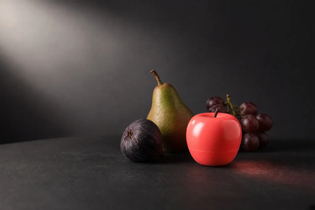 A wax fruit among real fruit, the fake one lit coral pink.