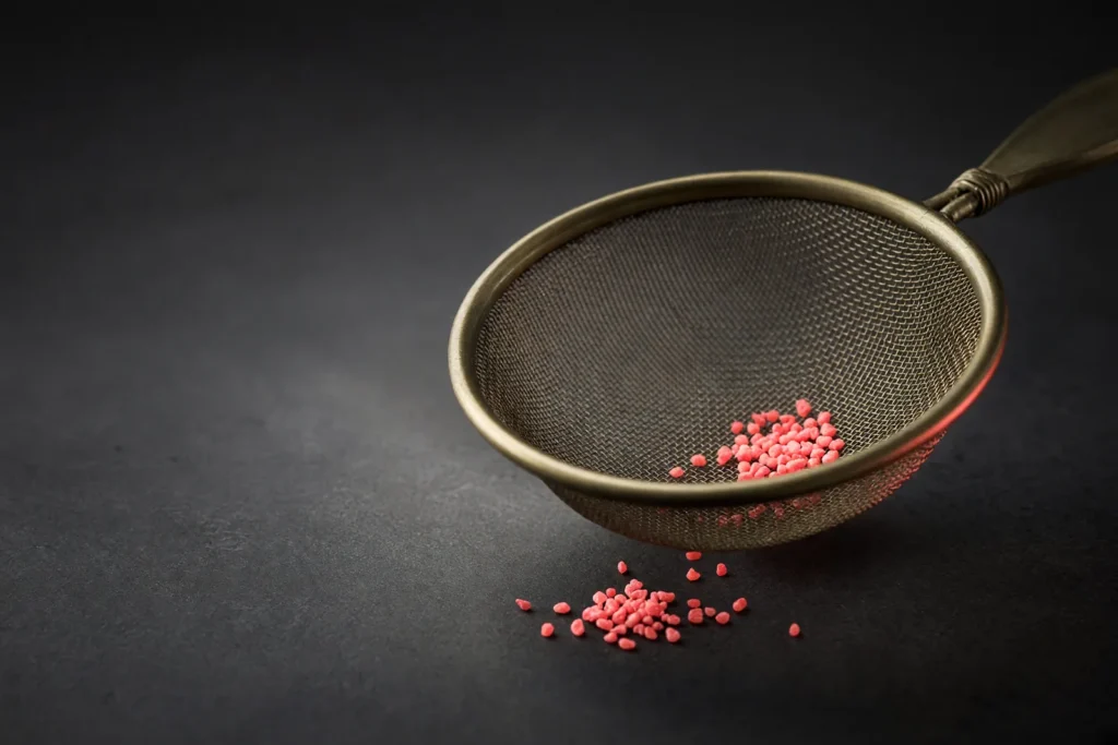 A brass sieve with a few glowing coral grains left in it.